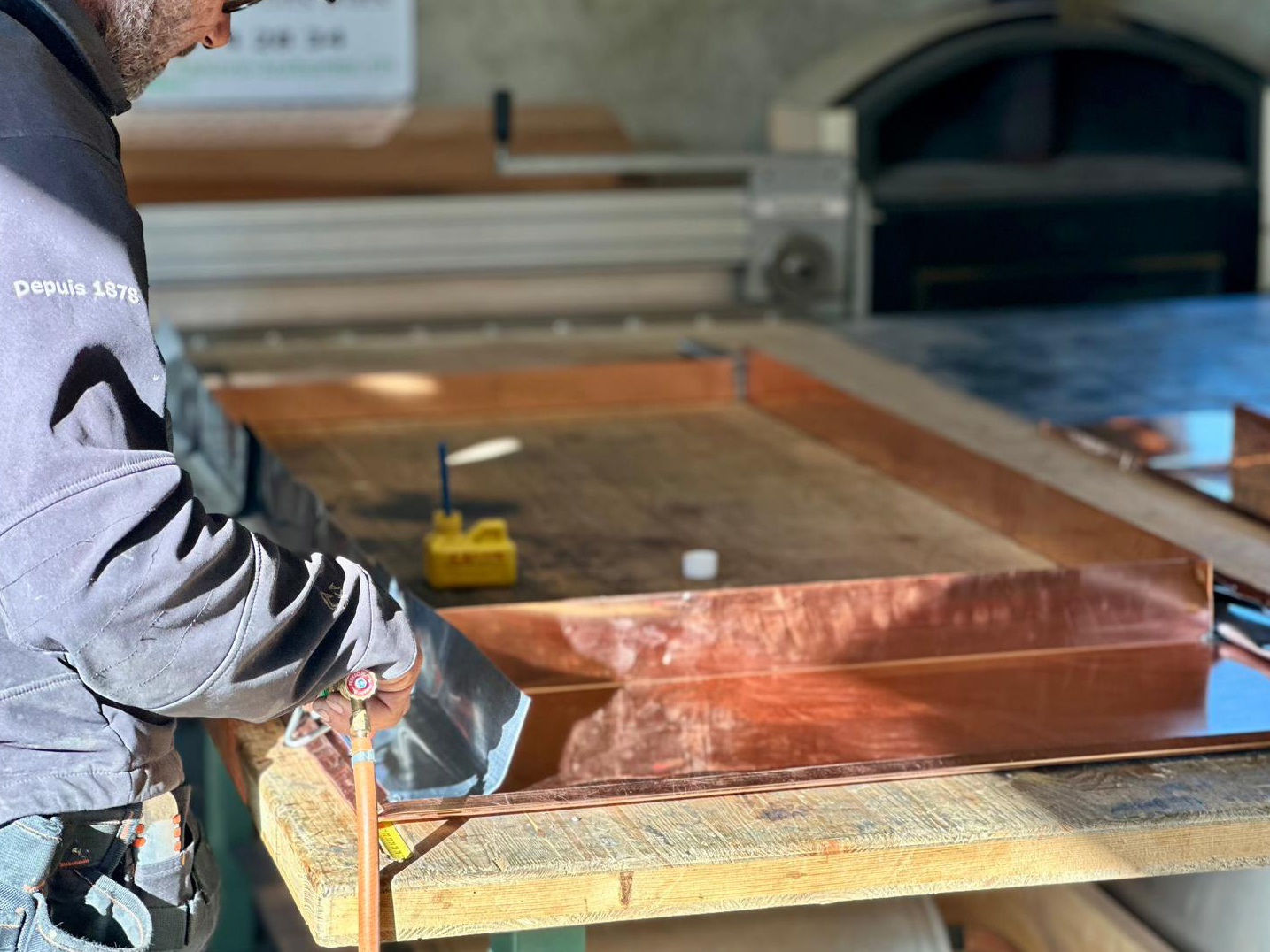 Artisan ferblantier façonnant une pièce en cuivre dans l'atelier Fahrni